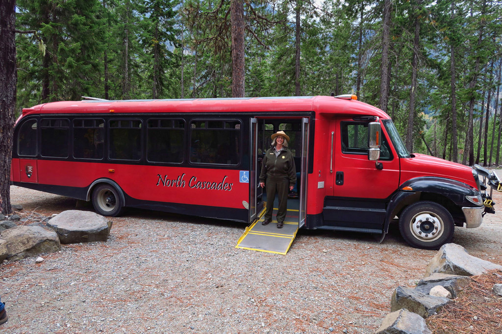 Park Ranger at the side of a red North Cascades tour bus.