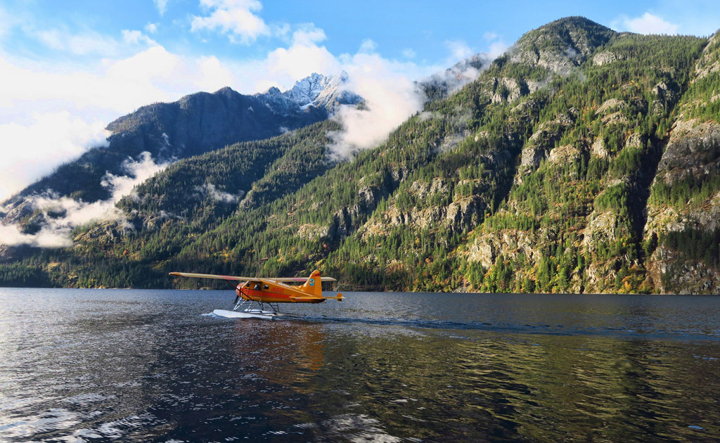 Small plane preparing to take off from the water with mountains lining the shoreline.