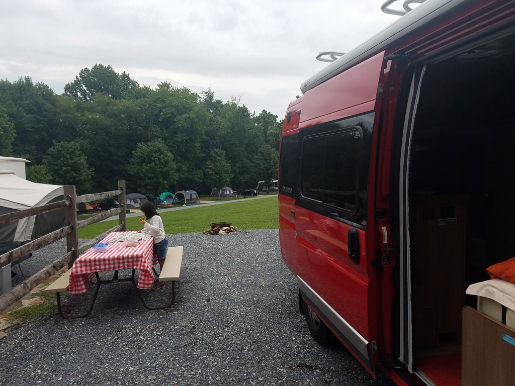 Winnebago Travato parked at campground with side door open and picnic table right out front