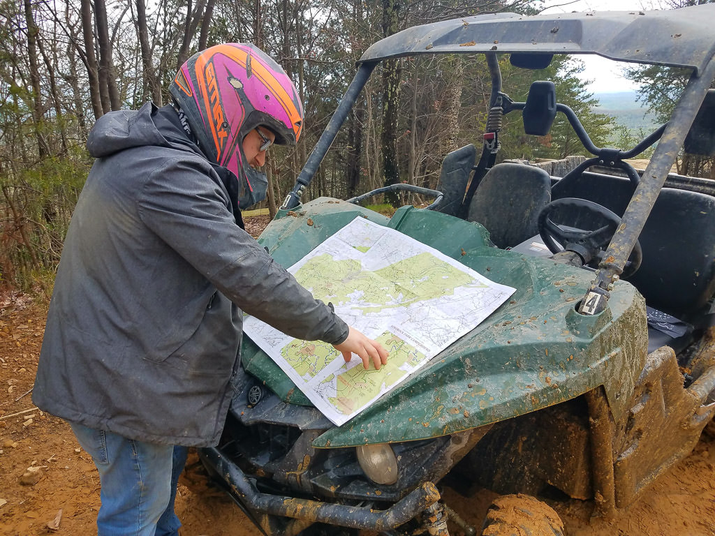 Man looking at a map resting on front end of muddy ATV